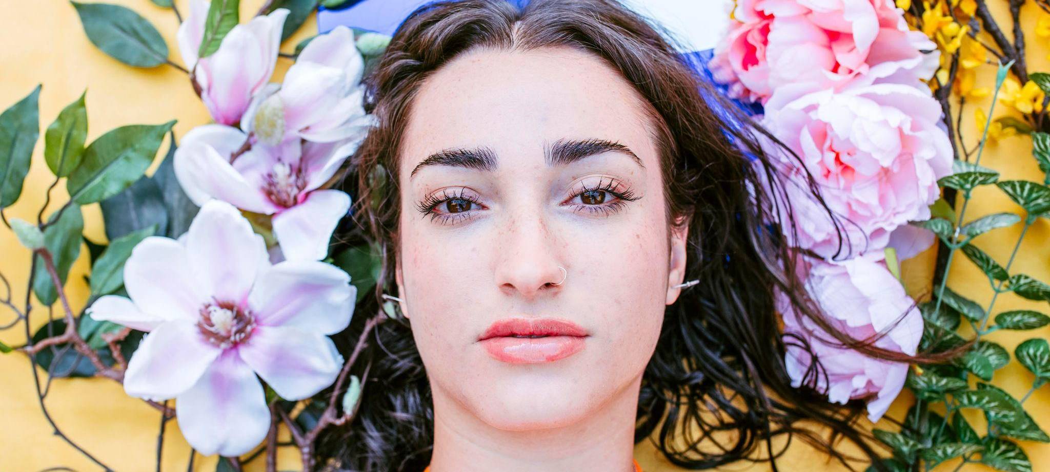 Natürlich geschminkte Frau liegt neben Blumen