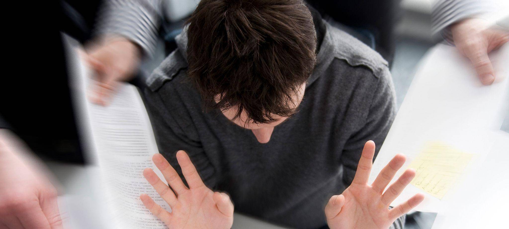 Mann mit hoher Arbeitsbelastung hebt im Büro abwehrend die Hände